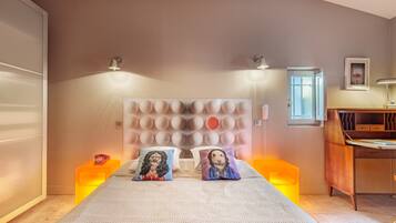 A bedroom with a large bed, two bedside lamps, a wooden desk, and a window.