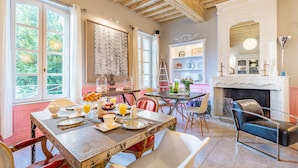 Un comedor con una mesa de madera dispuesta para el desayuno, una chimenea y vistas a la vegetación a través de amplias ventanas.