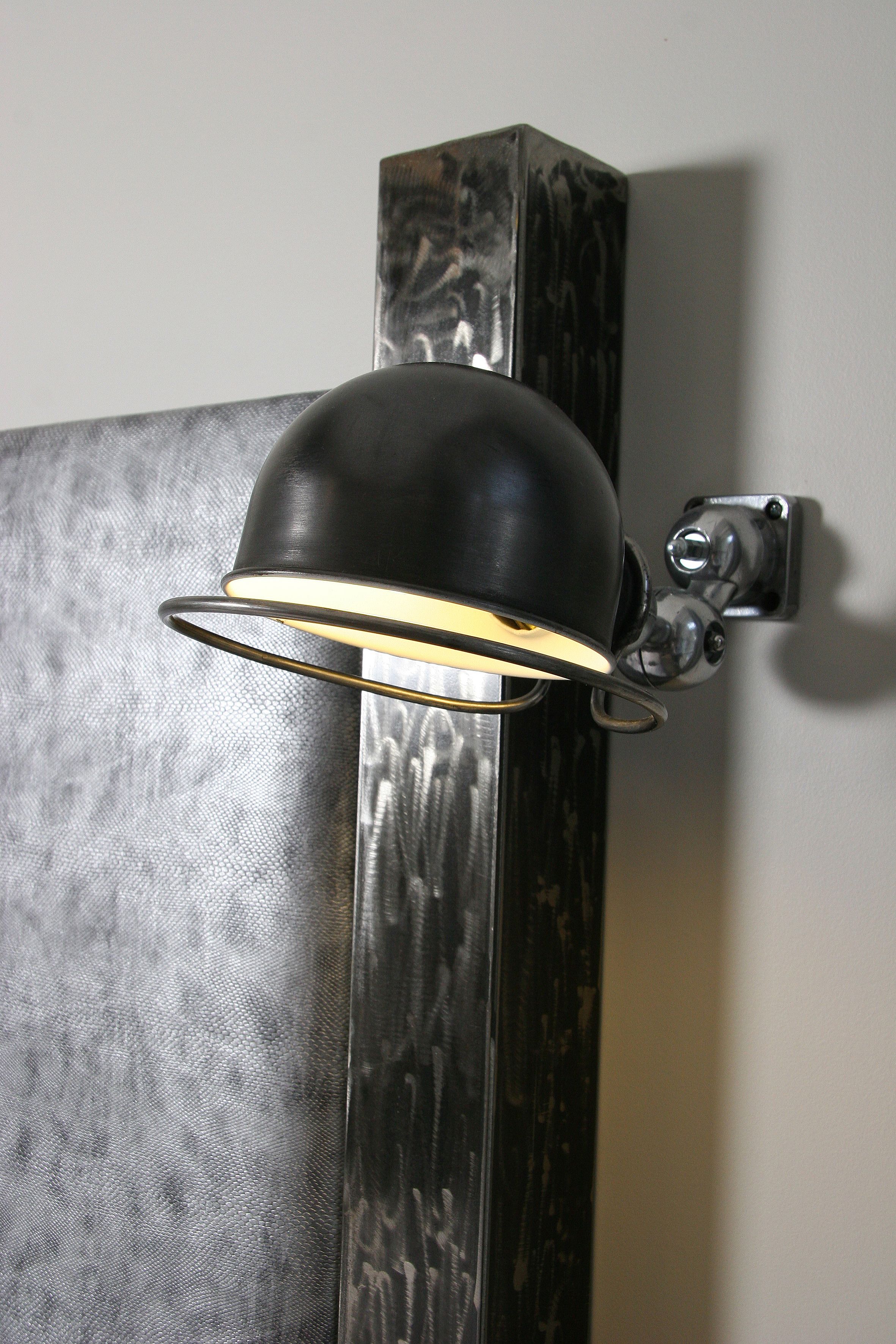 A wall-mounted lamp with a black shade and a metallic base, attached to a textured wall.