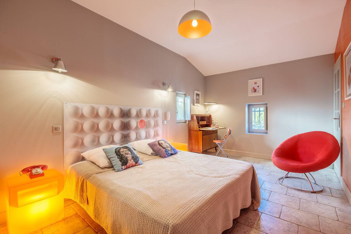 Une chambre à coucher avec un grand lit, un bureau, une chaise rouge et un luminaire suspendu.