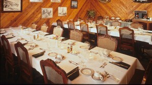 A dining area with multiple tables set for meals, wooden walls, and framed pictures on the walls.
