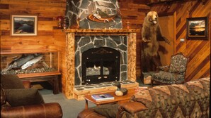 A cozy lodge interior with a stone fireplace, leather furniture, and a bear statue.