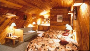 A cozy attic bedroom with wooden walls and ceiling, a floral bedspread, and two bedside lamps.