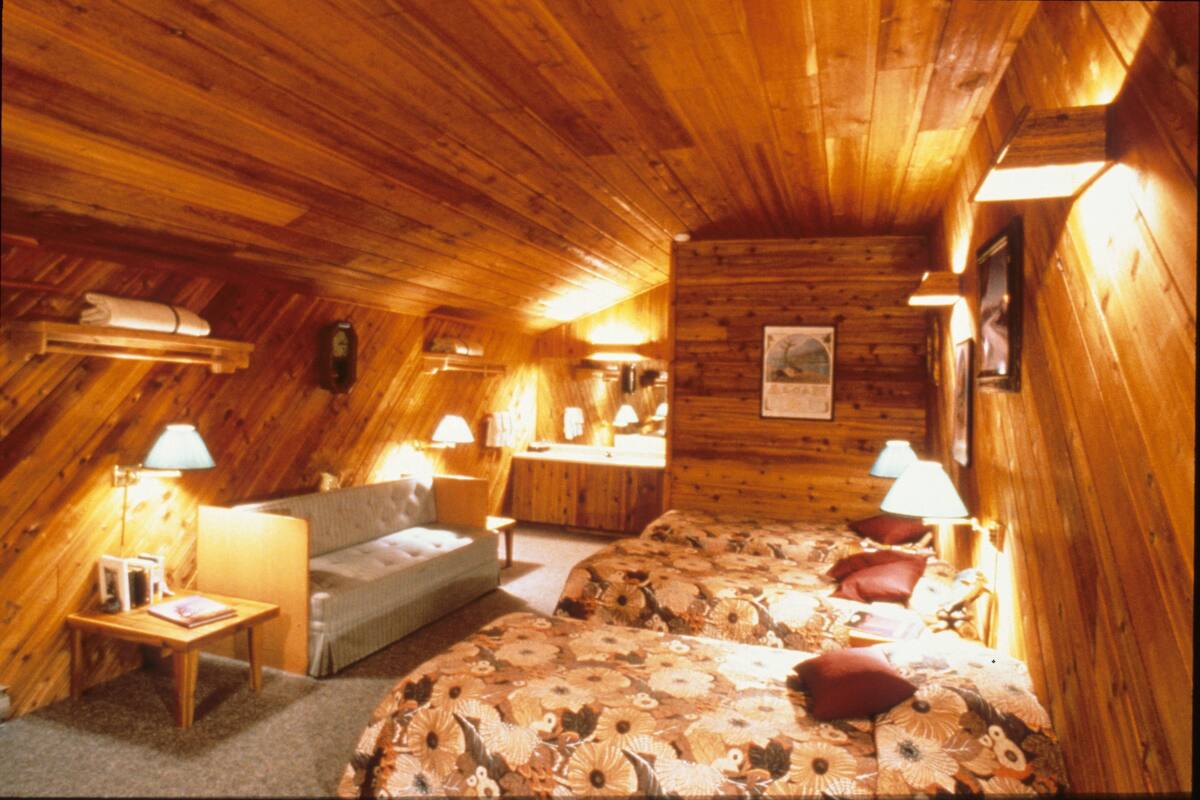 Une chambre confortable située sous les combles, avec des murs et un plafond en bois, une couvre-lit à motifs floraux et deux lampes de chevet.