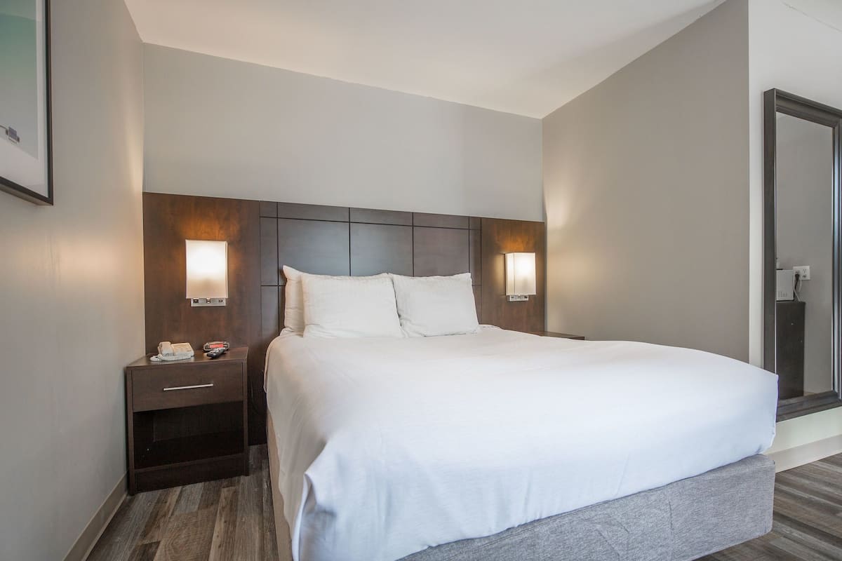 A hotel room with a large bed, a nightstand with a phone and a lamp, and a wall-mounted light fixture.