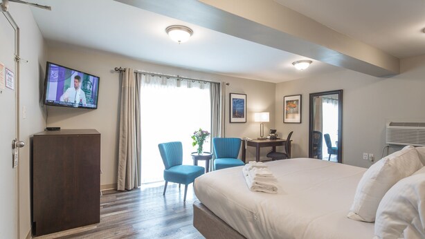 Habitación de hotel con una cama grande, un escritorio con silla, televisor montado en la pared y una ventana con cortinas.