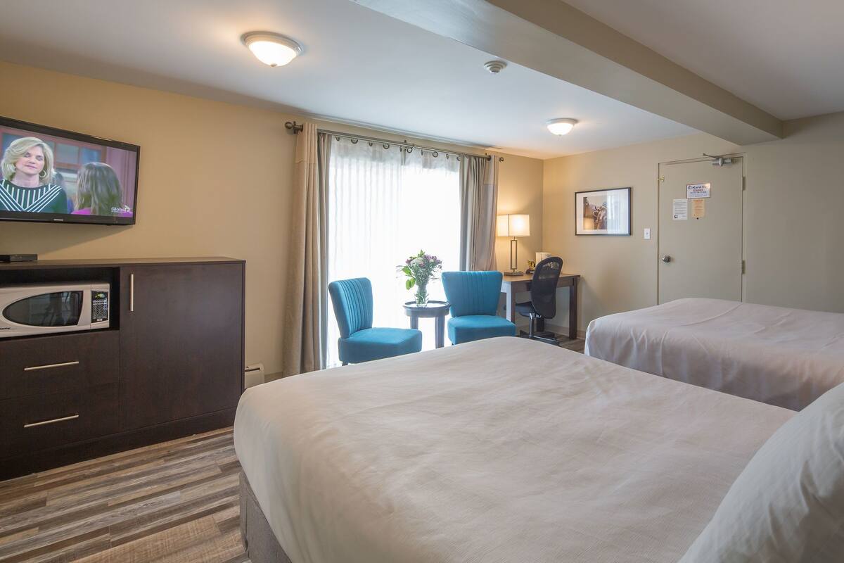 A hotel room with two beds, a desk, a chair, a TV, a microwave, and a window with curtains.