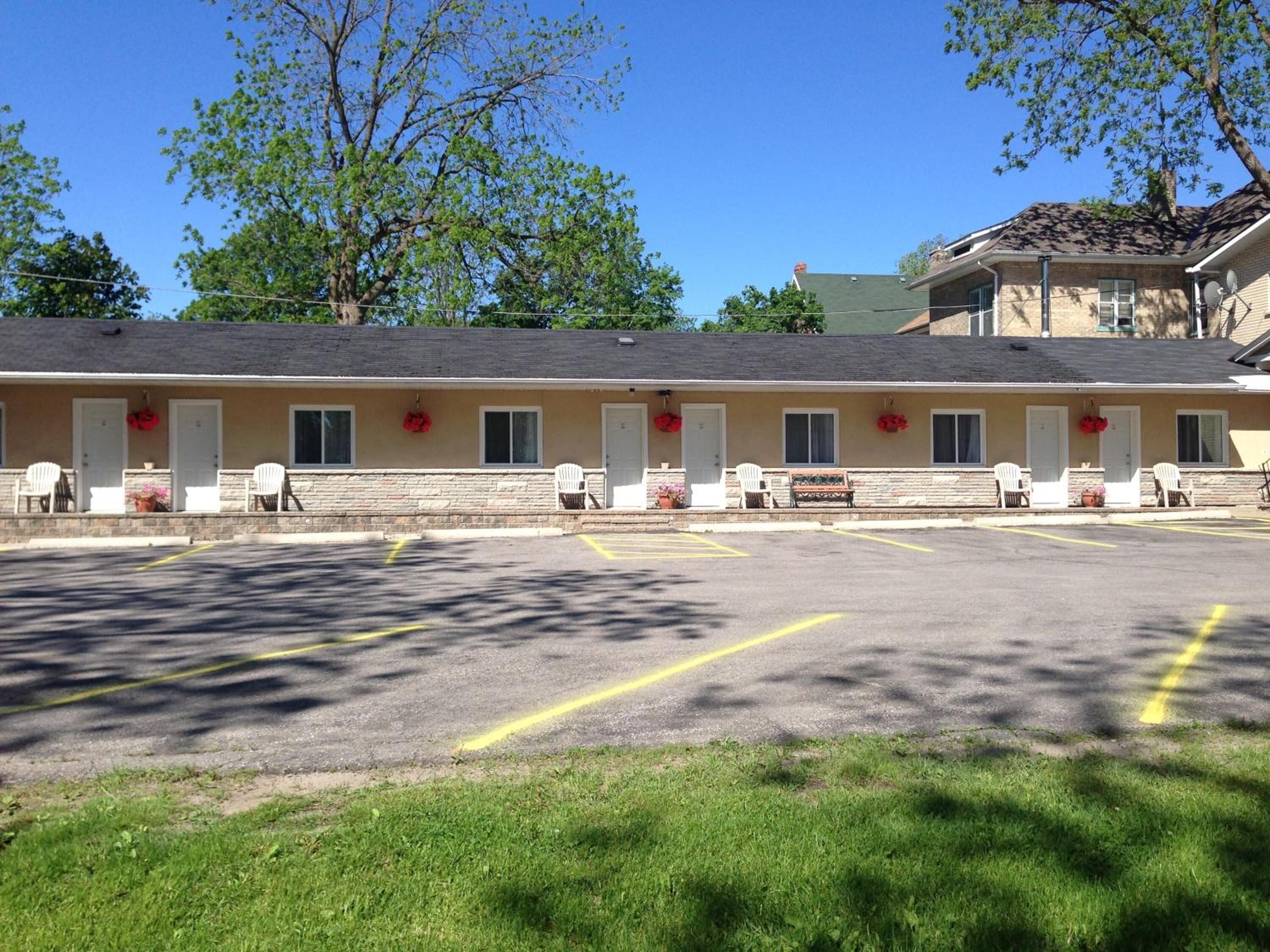 Un motel con una hilera de habitaciones, cada una con puerta y ventanas, y un estacionamiento al frente.