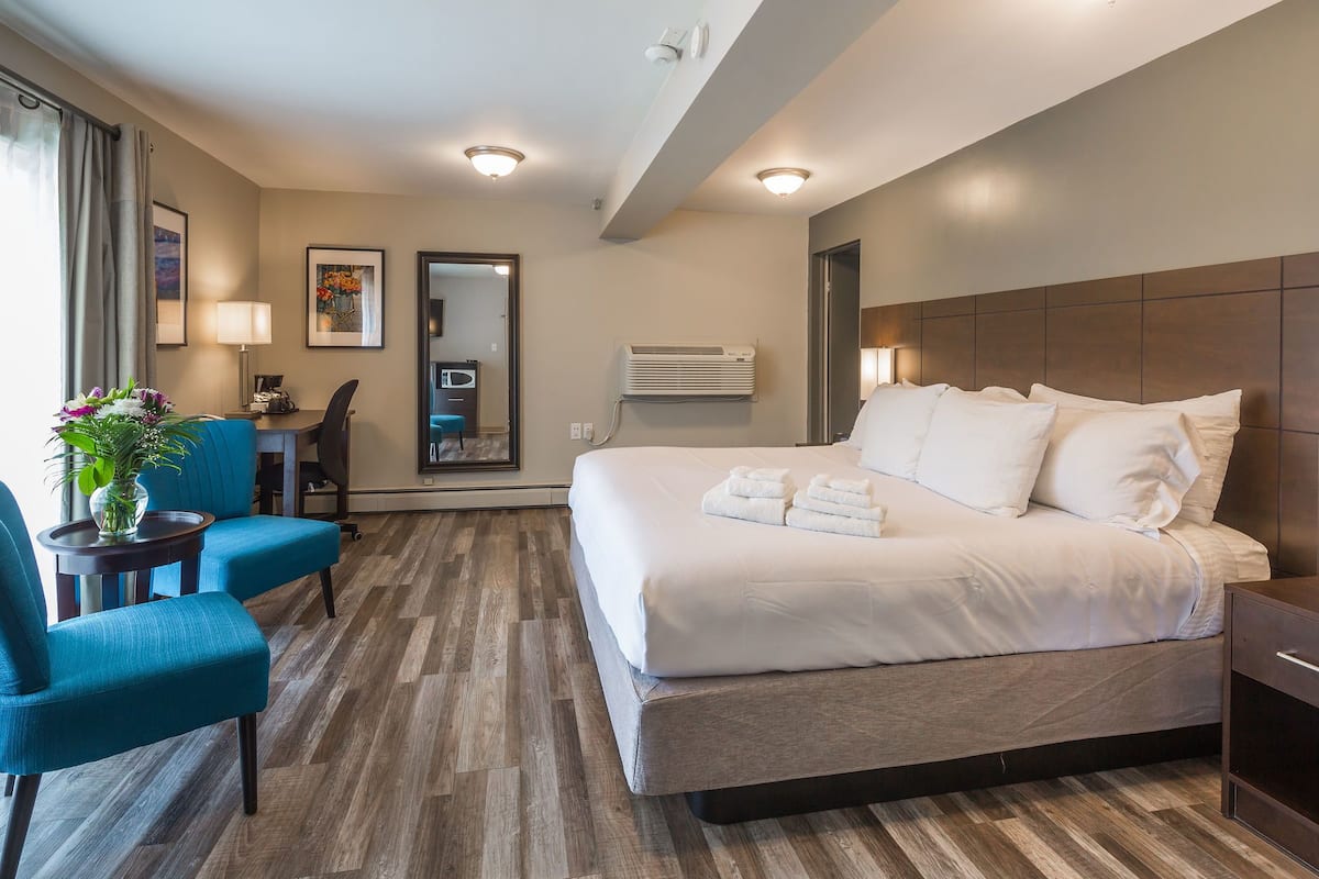 A hotel room with a large bed, a desk with a chair, a small table with a vase, and a mirror on the wall.