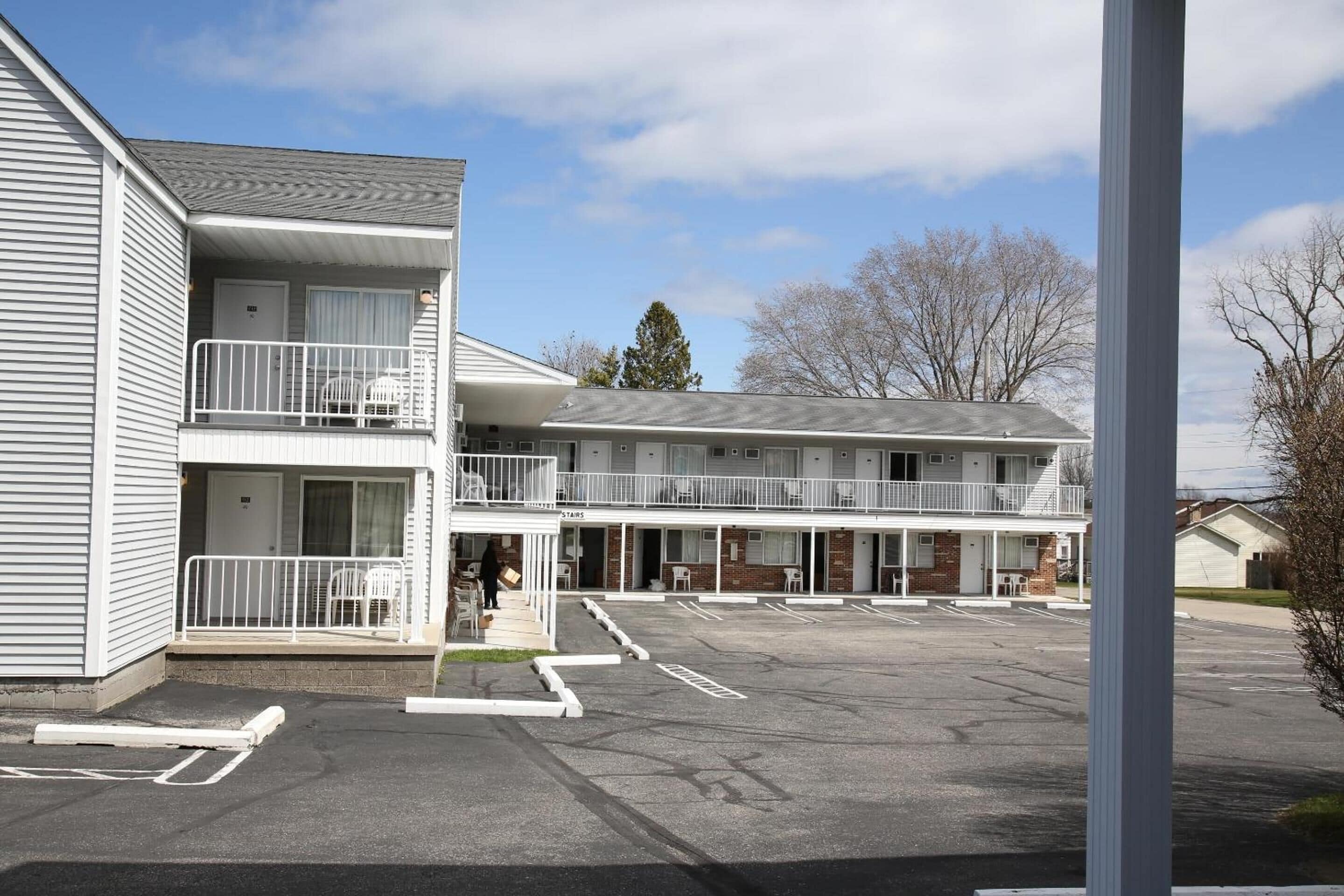 A multi-story motel with a parking lot and a covered outdoor seating area.