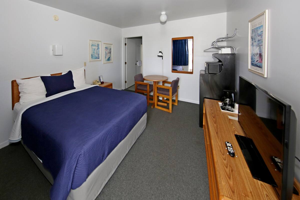 A hotel room with a large bed, a desk with a TV, and a chair.