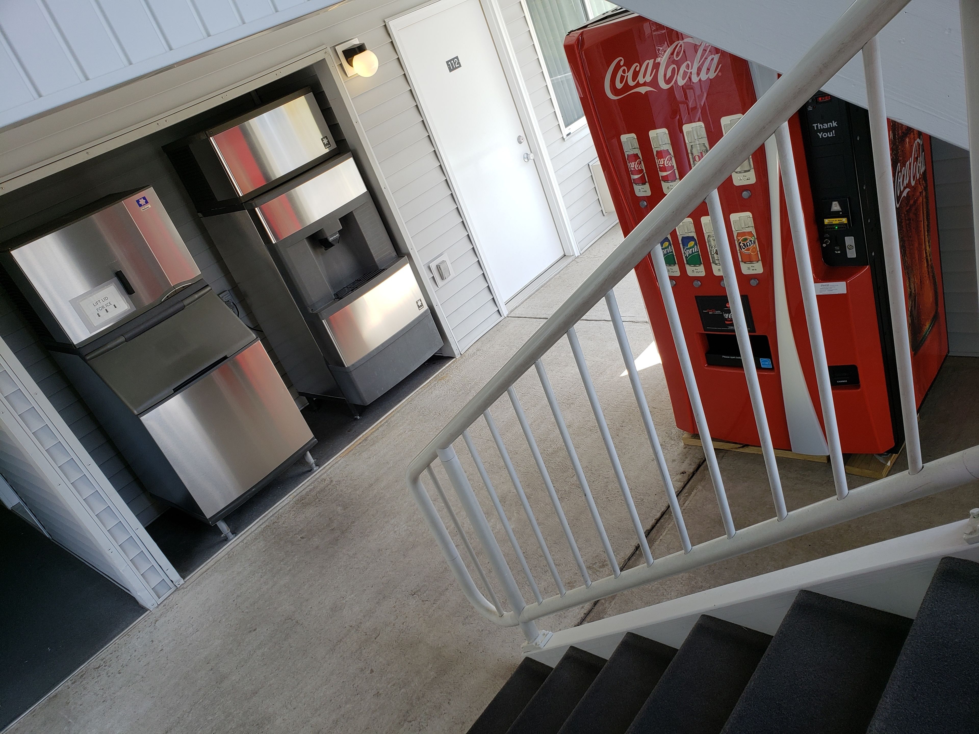 A staircase leading to a room with a refrigerator, a Coca-Cola vending machine, and a door marked with the number 112.