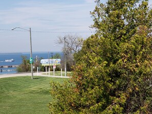 A grassy area with a sign for Mackinac Island Ferry, a body of water, and a distant view of a lighthouse. - Aurora Borealis Motel (St Ignace)