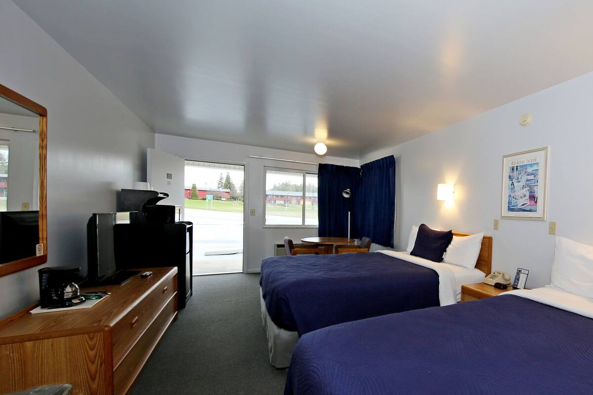 A hotel room with two beds, a desk with a computer, a TV, and a window with curtains.