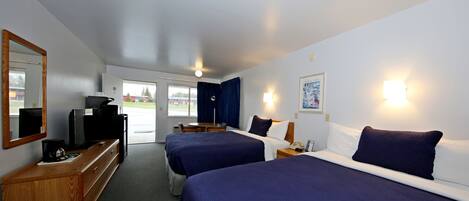 A hotel room with two beds, a desk with a computer, a TV, and a window with curtains.