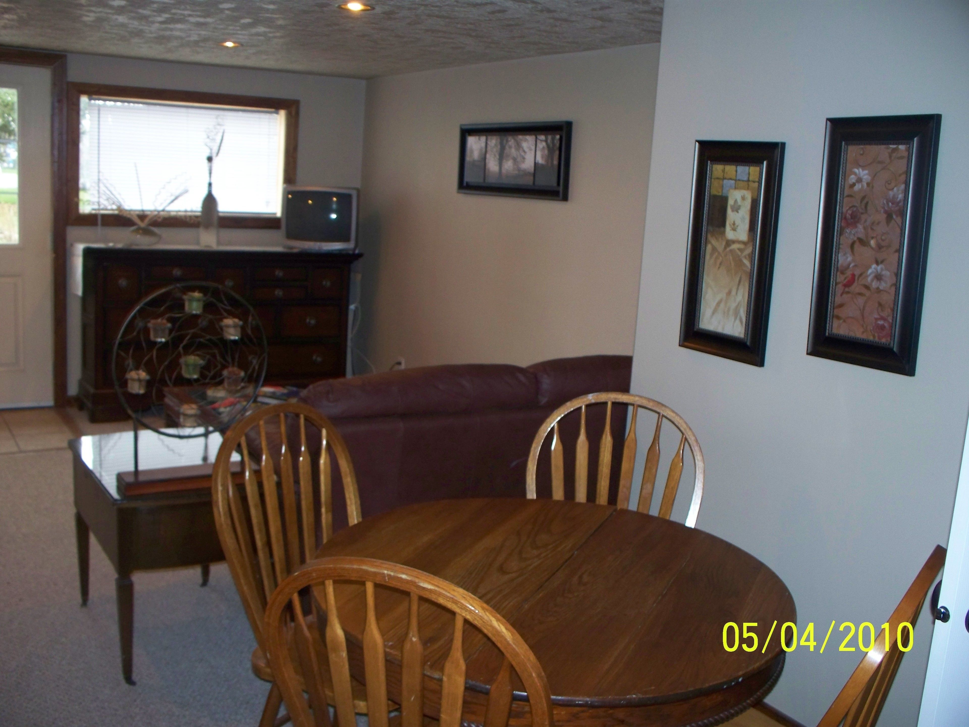 A dining area with a wooden table and chairs, a glass-top coffee table, a red sofa, and a television in the background.