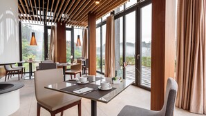 A modern dining area with a glass table, chairs, and a view of a mountainous landscape.