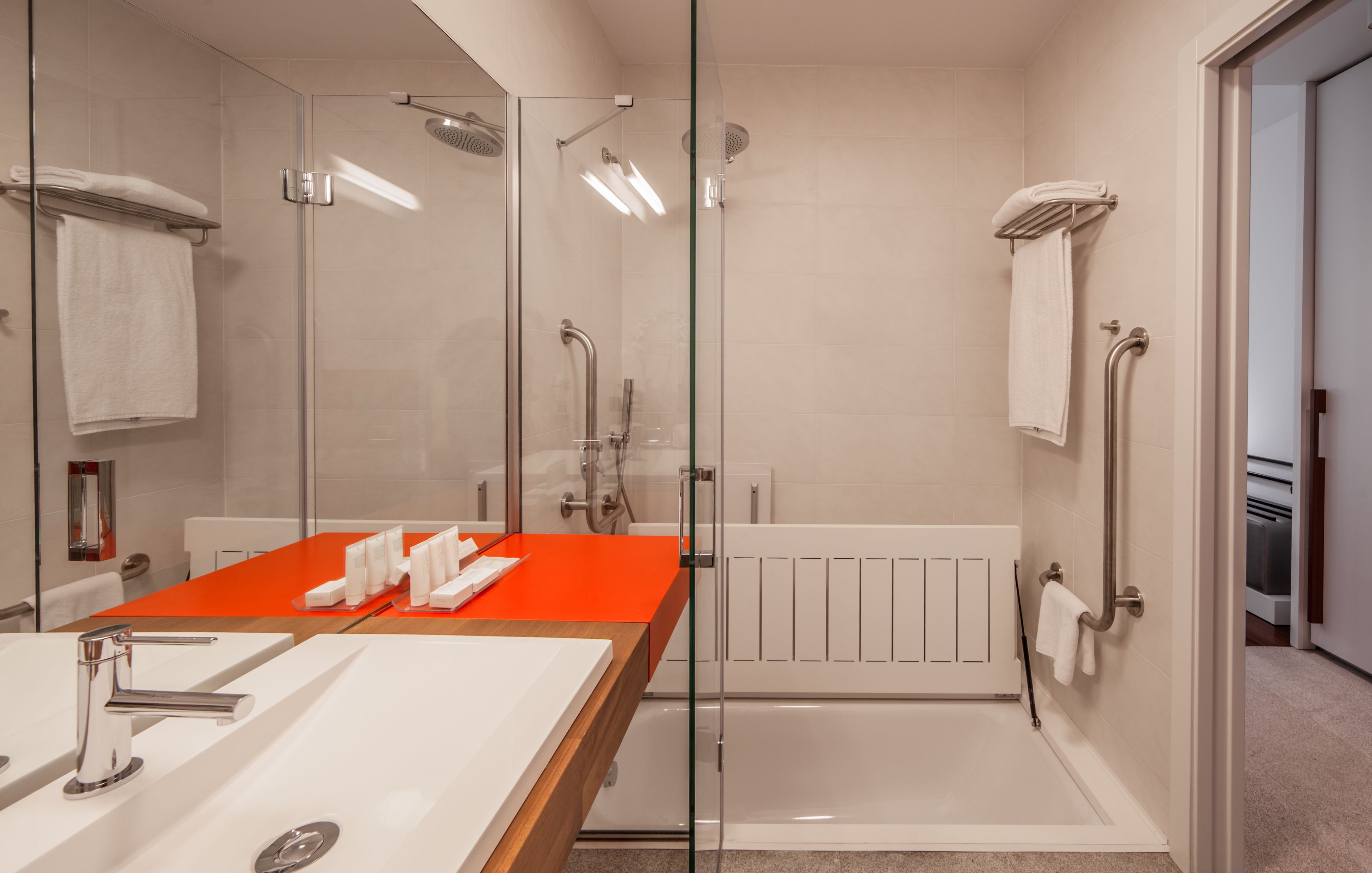 A modern bathroom with a glass shower enclosure, a white bathtub, and a red countertop.