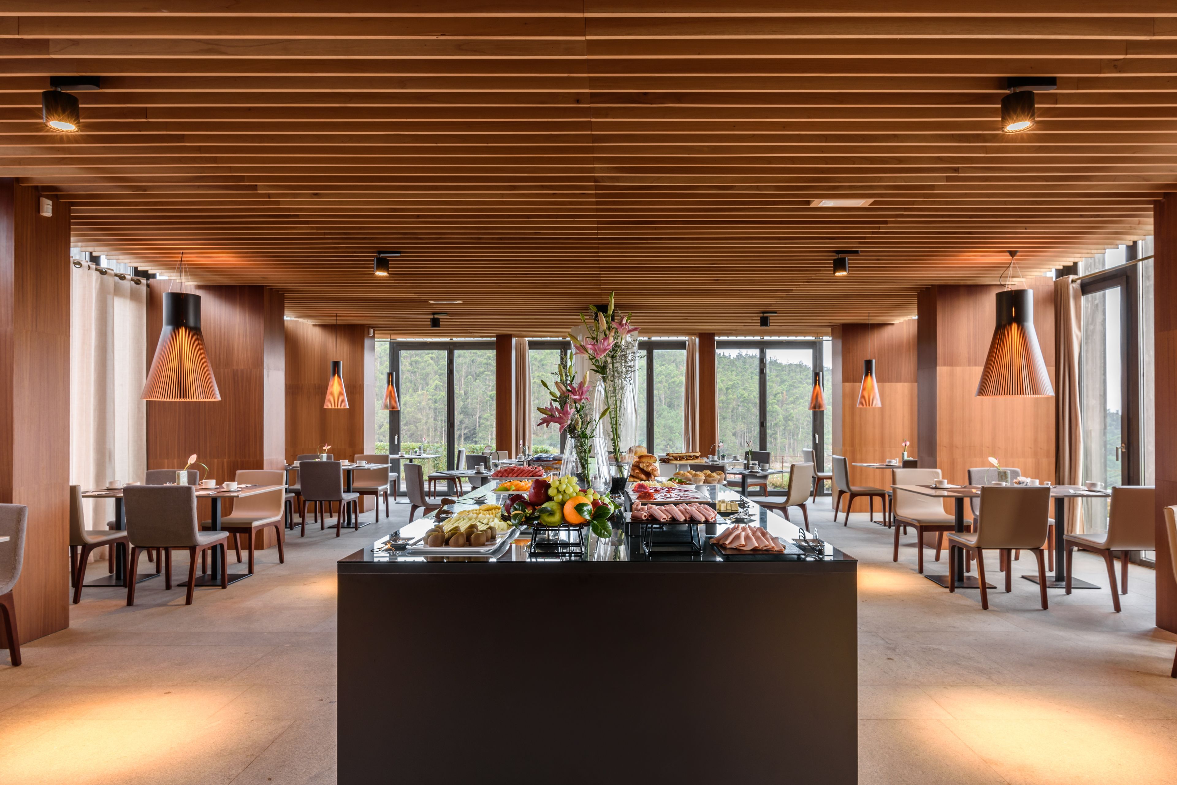 Un comedor moderno con paneles de madera, ventanas amplias y una mesa buffet central.