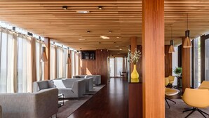 A modern hotel lobby with wooden panel ceilings, grey sofas, yellow chairs, and a large vase with flowers.