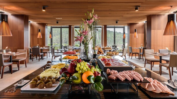 A buffet setup in a modern dining area with wooden ceiling and large windows.