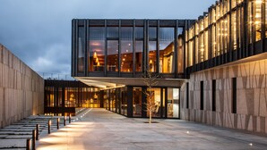 A modern building with a glass facade, a covered walkway, and a tree in the center.