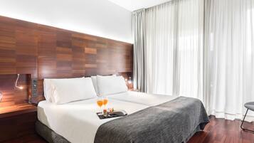 Habitación de hotel moderna con una cama grande, cabecera de madera y vistas de la ciudad a través de cortinas translúcidas.