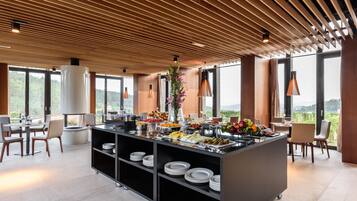 Un amplio bufé de desayuno moderno con diversas opciones de comida, un arreglo floral central y vistas al exterior a través de grandes ventanales.