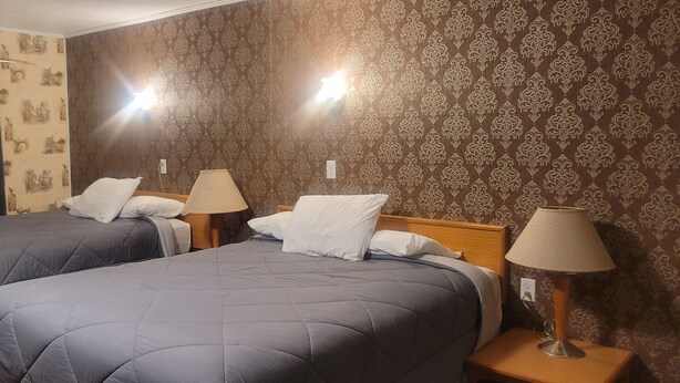 A hotel room with two beds, each with a pillow and a lamp on a bedside table. - Neepawa motel (Neepawa)