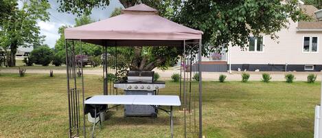 Een prieel met een tafel en een grillset in een gazon.