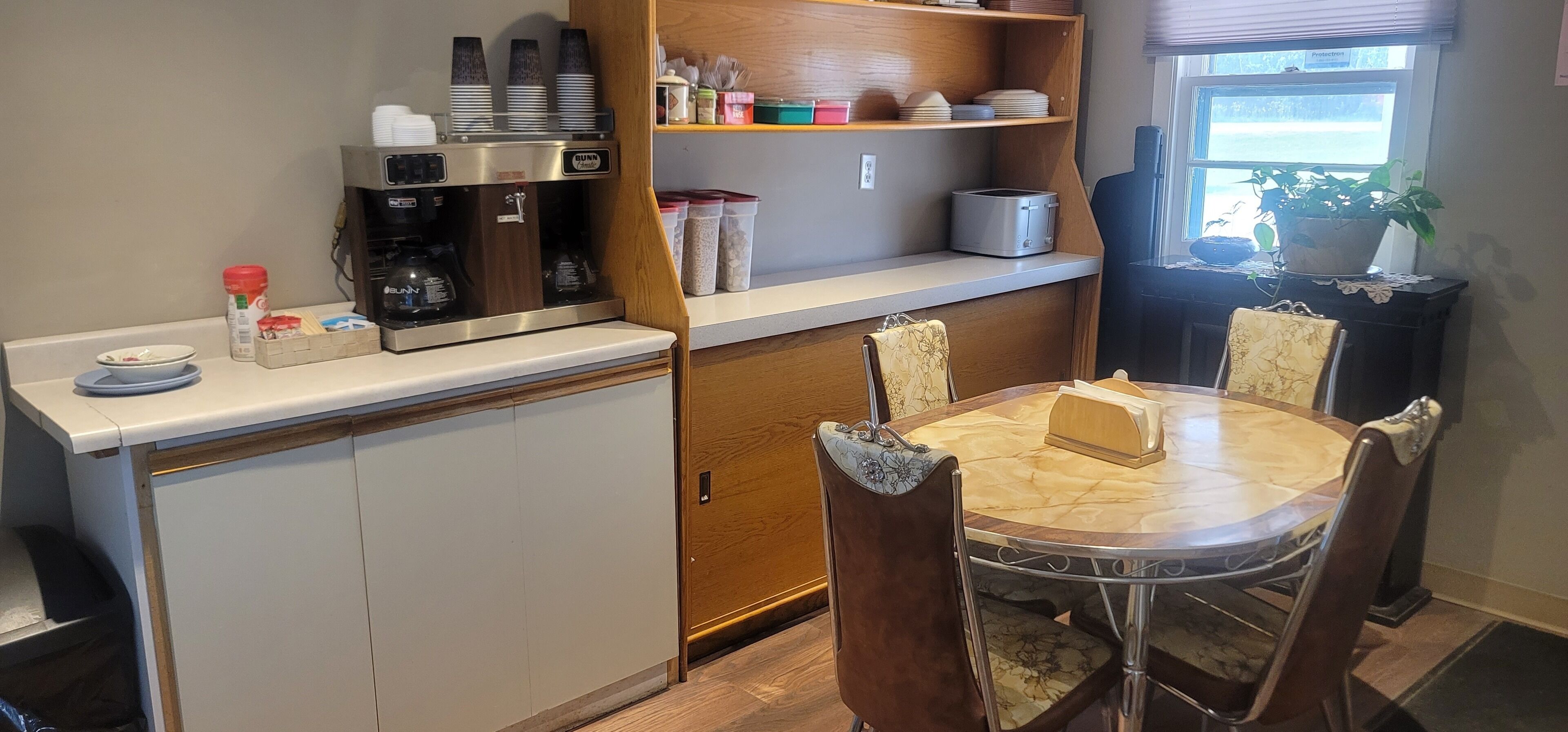 Een kleine keuken met een koffiezetapparaat, een broodrooster en een eethoek met een tafel en stoelen.