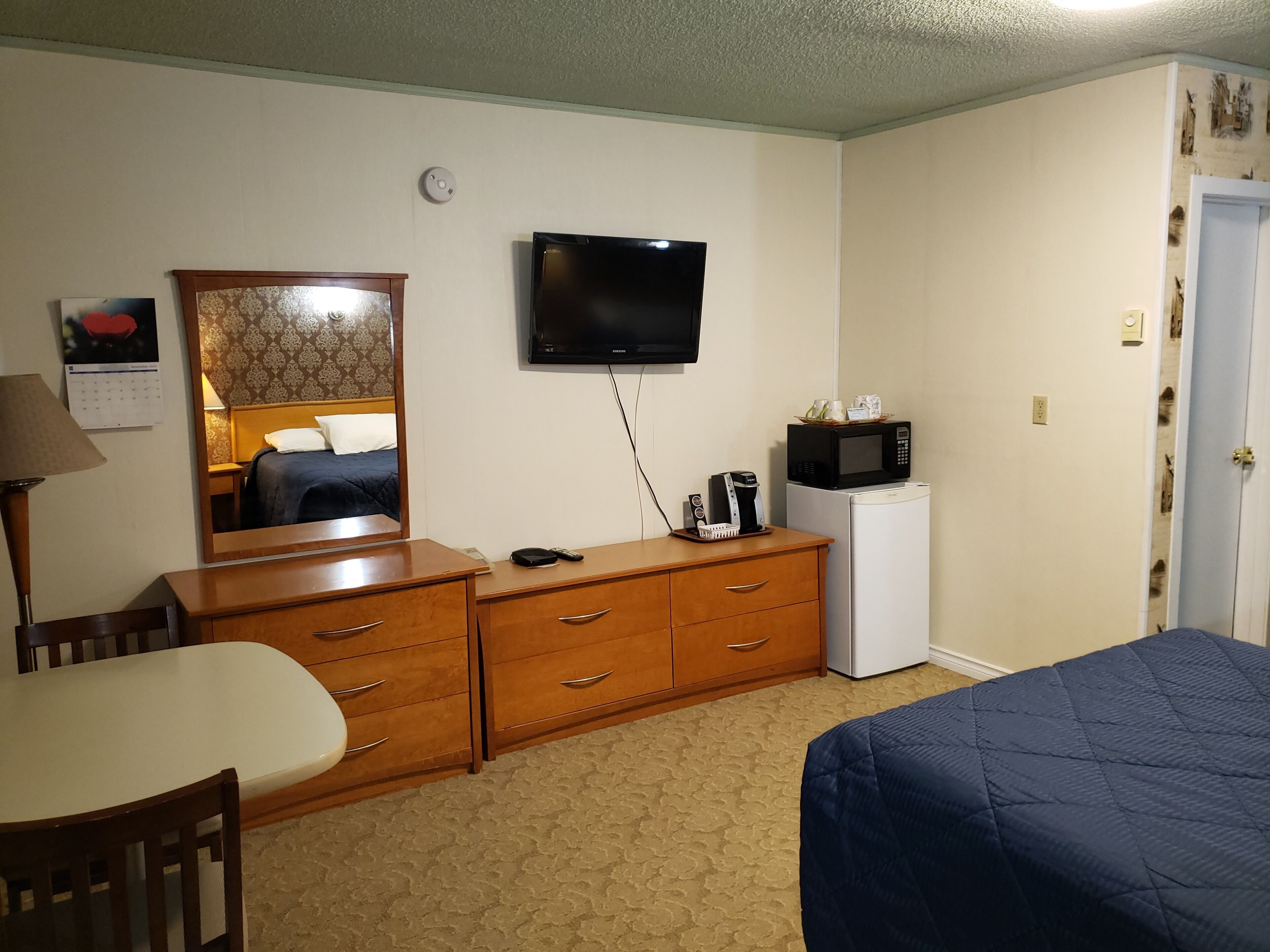 Una habitación de hotel con una cama, un escritorio, un aparador, un televisor, un microondas y un calendario en la pared.