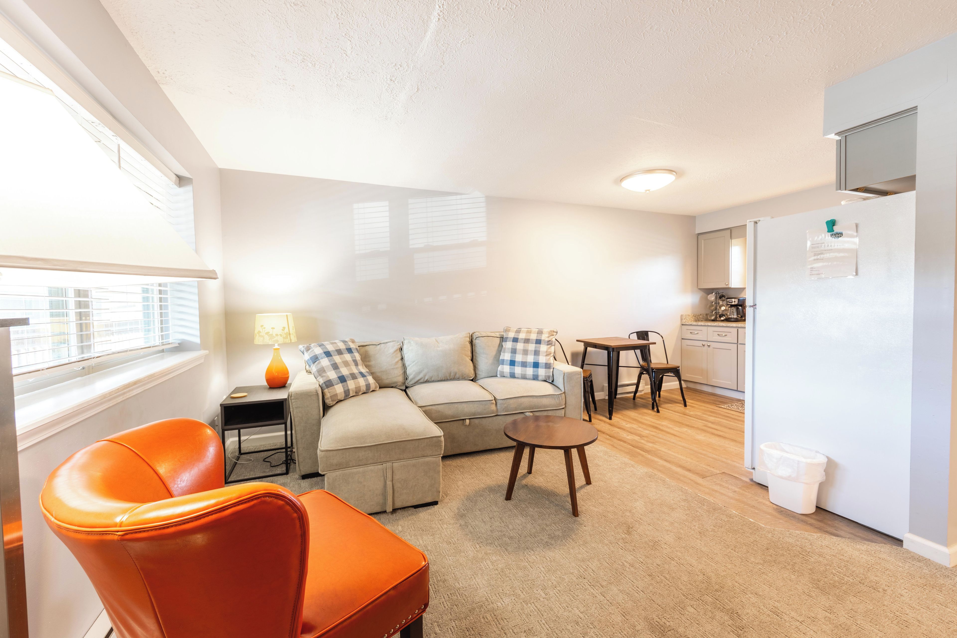 A compact living space with a sofa, a small table, a chair, a lamp, and a refrigerator.