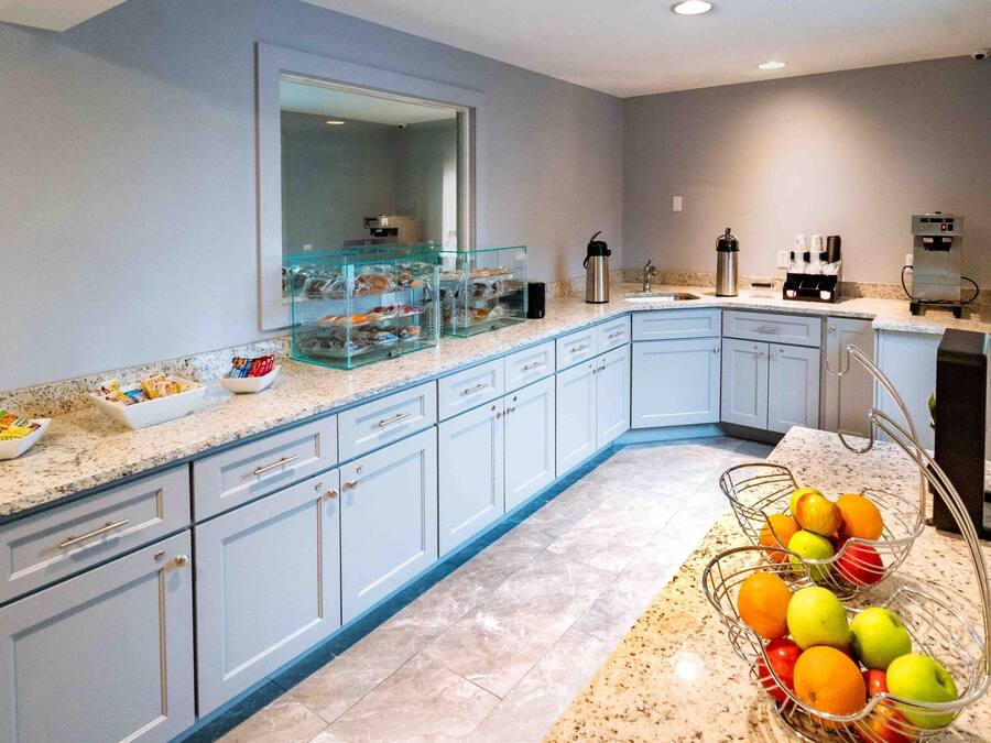 A modern kitchen with light blue cabinets, a marble countertop, and a fruit basket.
