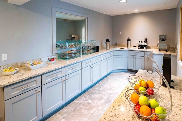 A modern kitchen with light blue cabinets, a marble countertop, and a fruit basket.