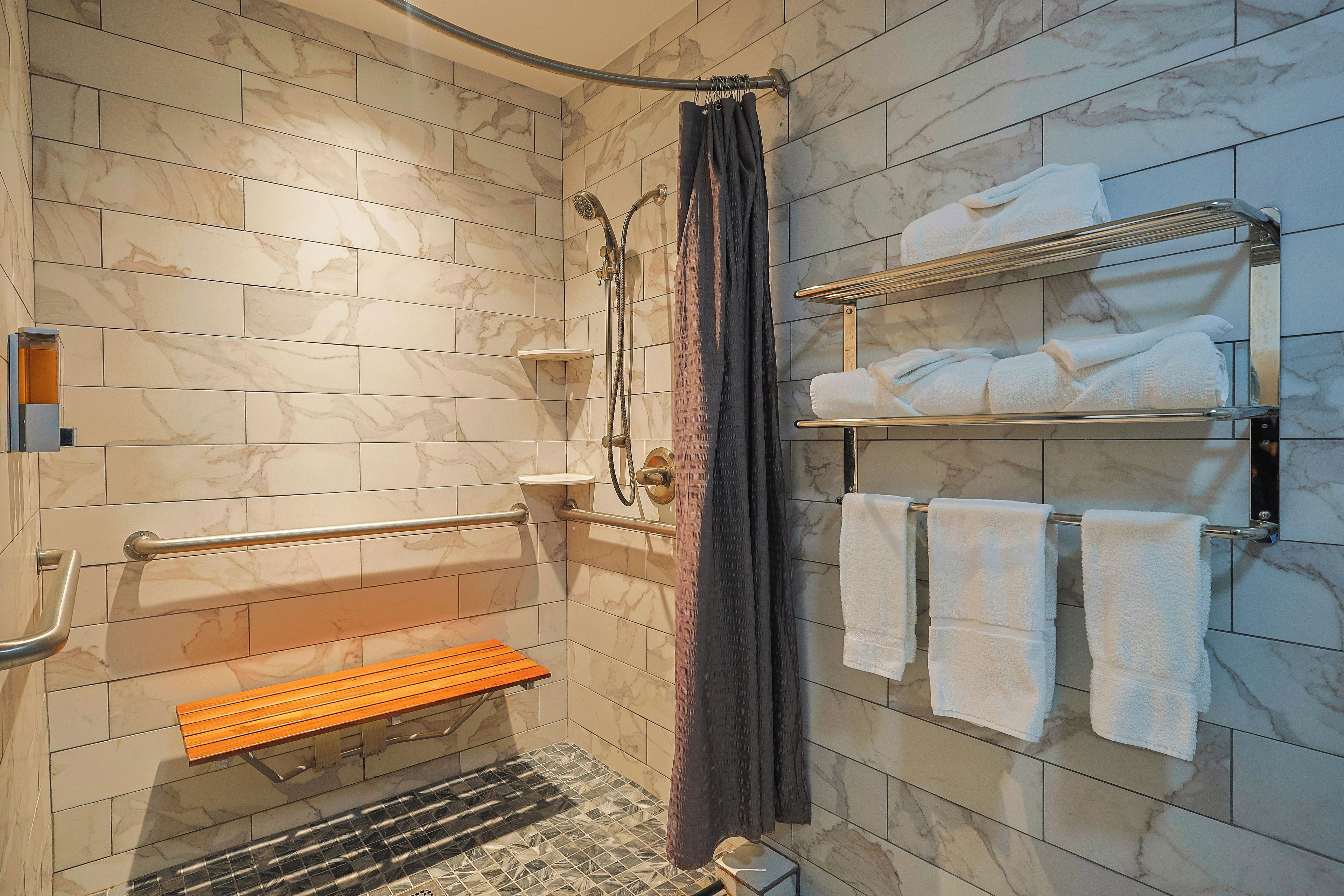A shower area with a handrail, a bench, a towel rack, and a showerhead.