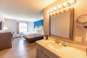 Hotelkamer met een groot bed, nachtkastje, spiegel, wastafel en raam met gordijnen.