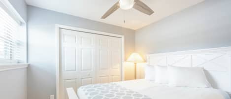 A bedroom with a bed, a ceiling fan, a nightstand, and a window with blinds.