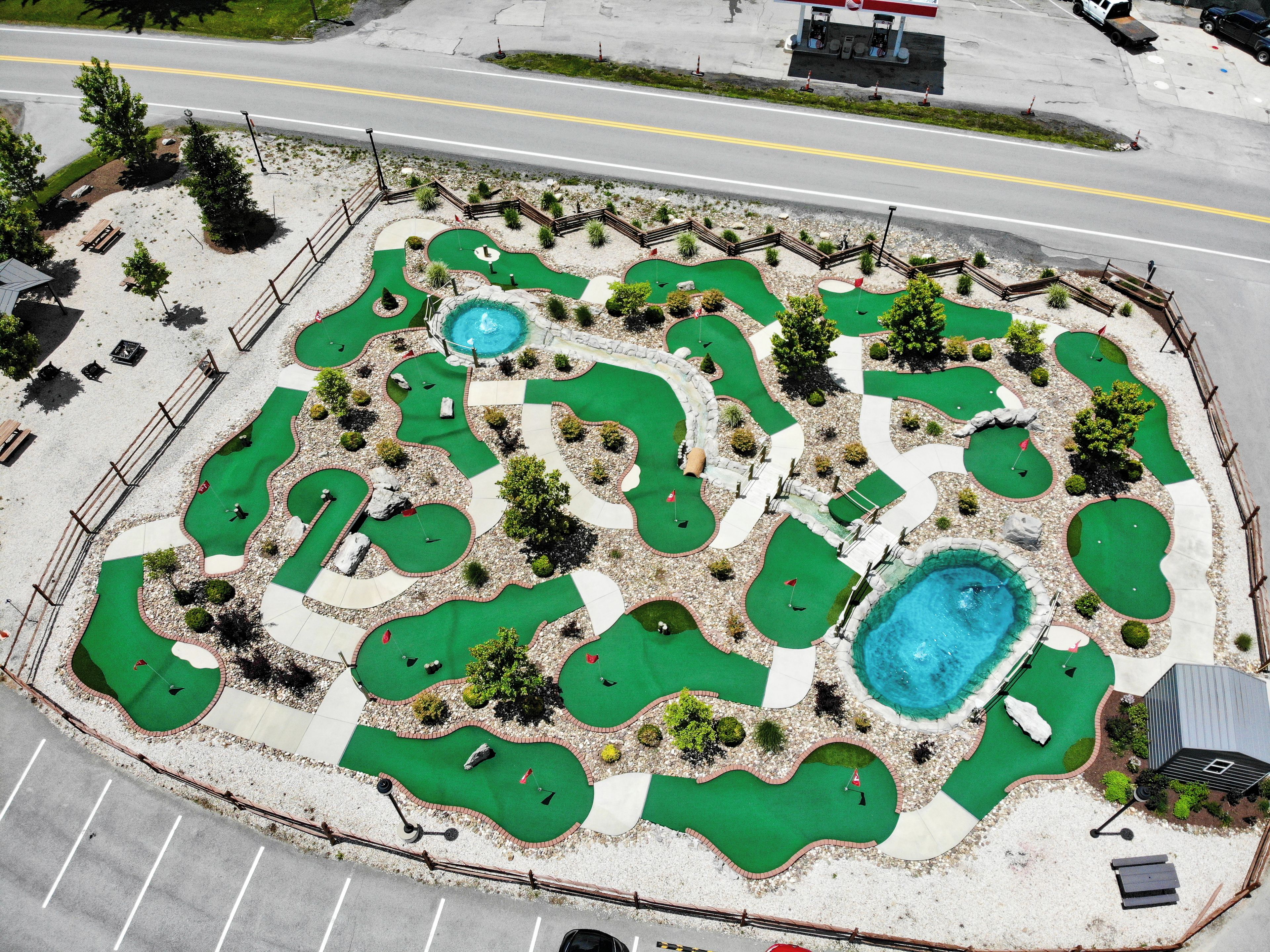 An aerial view of a miniature golf course with multiple holes, a small pool, and surrounding landscaping.