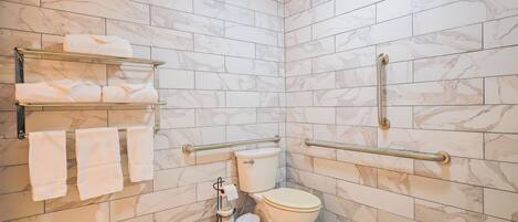 A bathroom with marble tiles, a toilet, a hand dryer, and a towel rack.