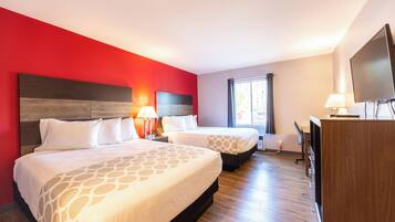 Habitación de hotel con dos camas, un escritorio, un televisor y una ventana con cortinas.