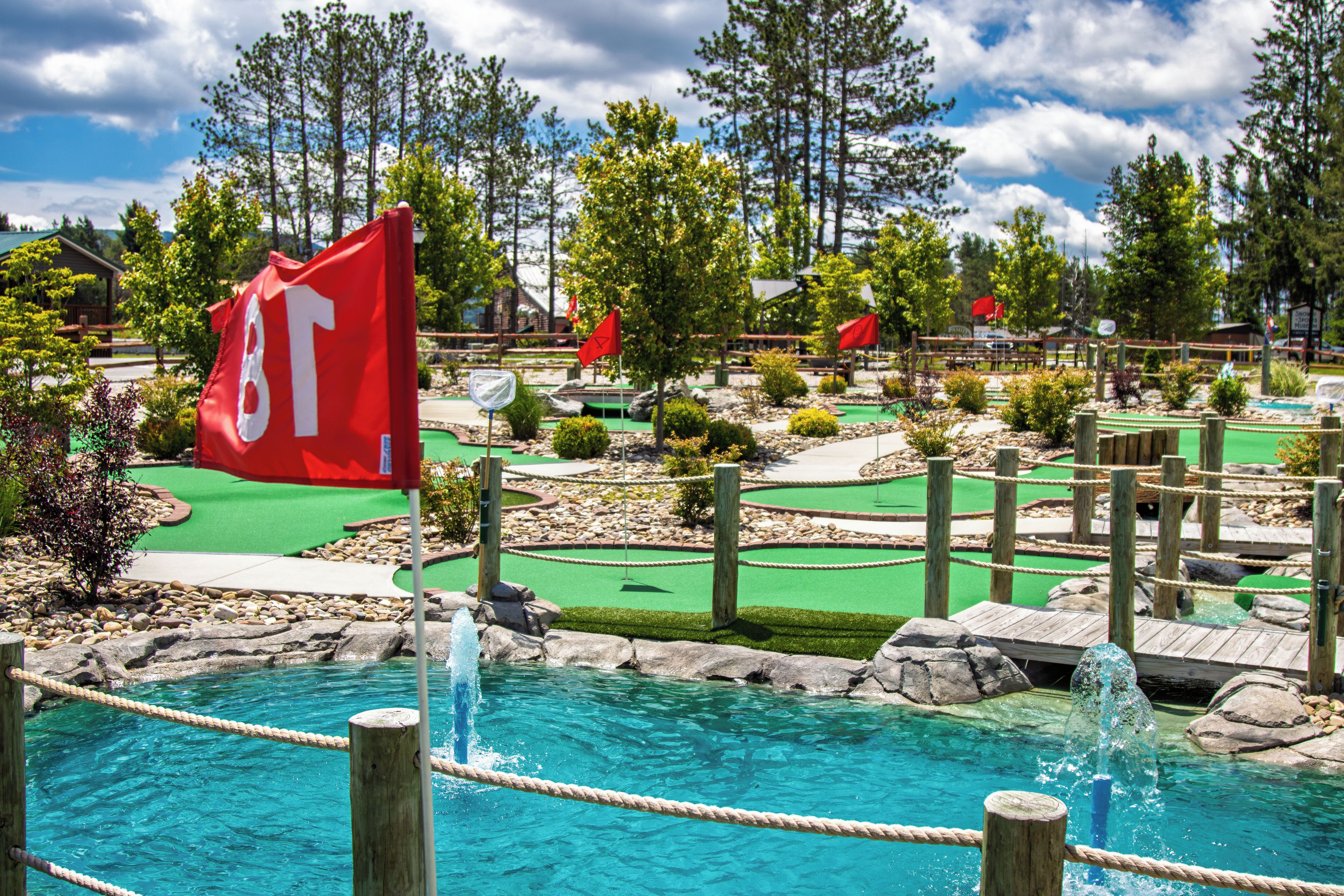 A miniature golf course with a flag, water features, and a wooden bridge.