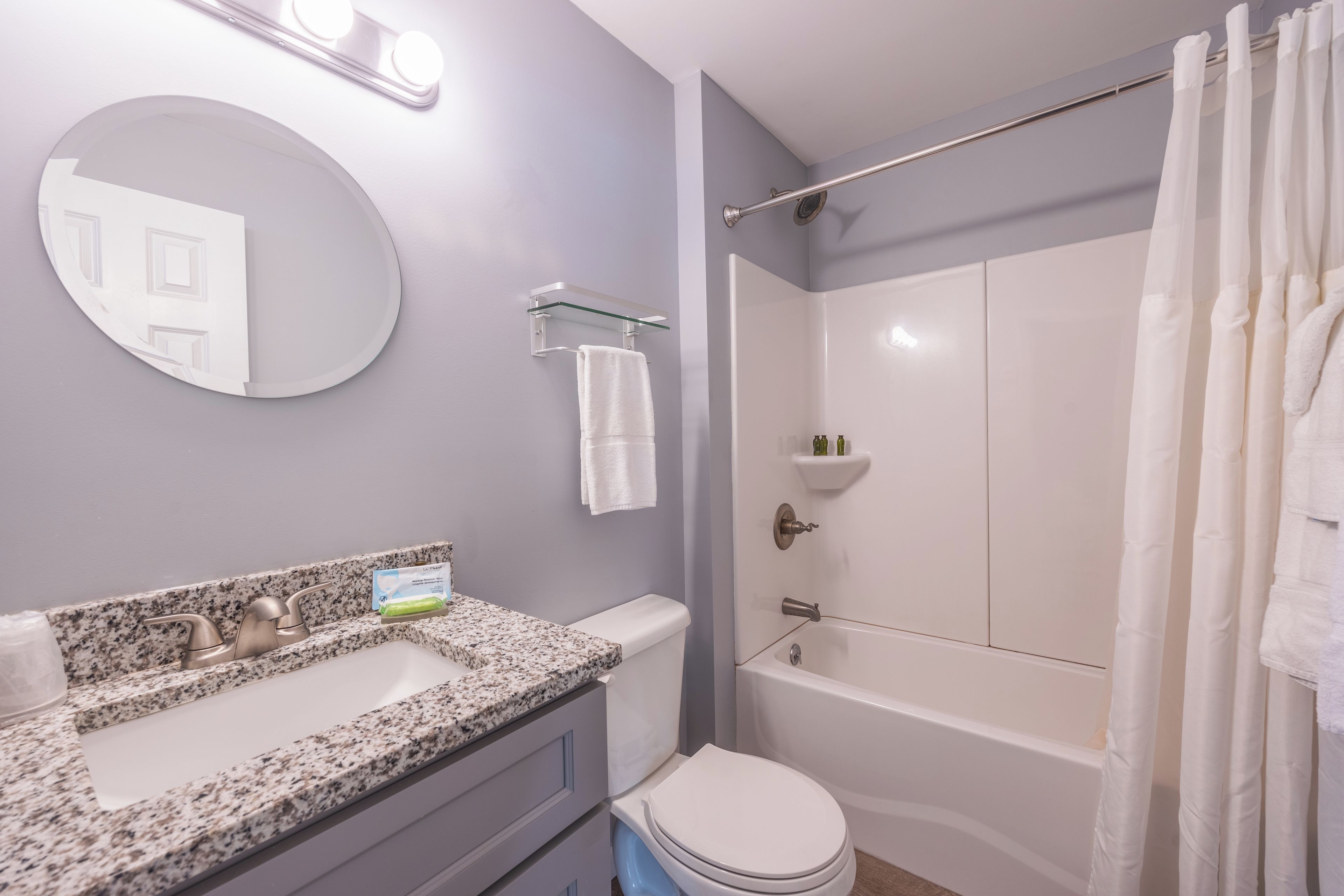 A bathroom with a granite countertop sink, a toilet, a bathtub, and a shower curtain.