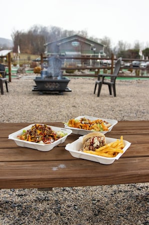 Een houten tafel met drie bakken, een barbecue en een gebouw op de achtergrond.