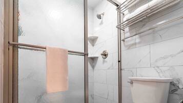 A bathroom with a glass-enclosed shower, a toilet, and a marble-tiled wall.