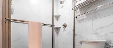 Kylpyhuone, jossa on lasiseinällä varustettu suihku, wc ja marmorilaatoilla päällystetty seinä.