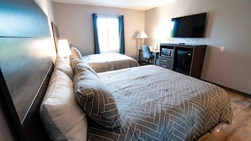 Ein Hotelzimmer mit zwei Betten, einem Schreibtisch mit Stuhl, einem Fernseher und einem großen Fenster mit Vorhängen.