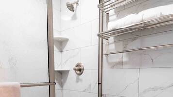 A bathroom with a glass-enclosed shower, a toilet, and a towel rack with towels.
