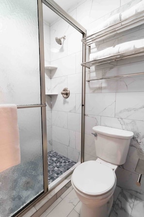A bathroom with a glass-enclosed shower, a toilet, and a towel rack with towels.