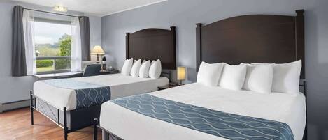 A hotel room with two beds, a ceiling fan, a window with curtains, and a view of greenery.
